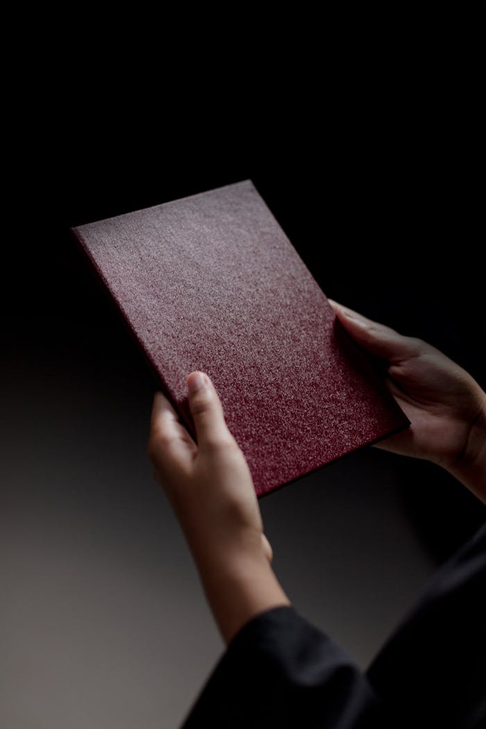 A person holds a red diploma cover, symbolizing graduation success.